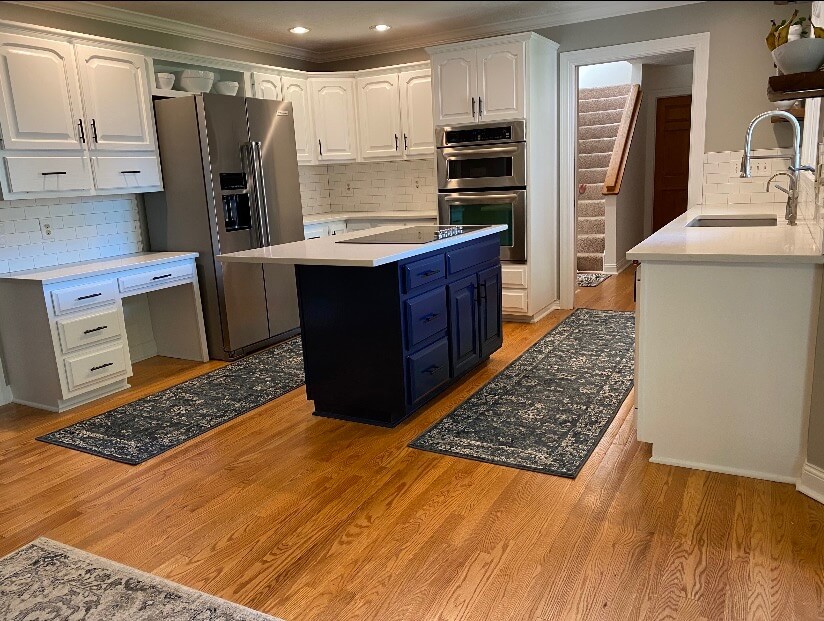 Interior kitchen with freshly painted white cabinets, blue island, hardwood floors, and modern appliances in a Zionsville home.